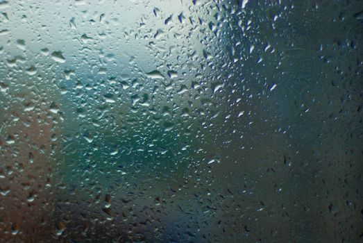 Close-up of raindrops on a glass window creating a blurred, abstract effect.