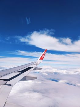 View from an airplane window showing a wing above fluffy clouds, over Sabah, Malaysia.