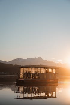 A serene morning scene with a boat reflecting on calm waters as the sun rises over a lake.