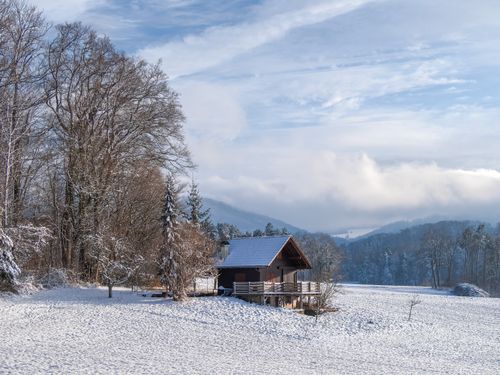 Free Beautiful snowy winter landscape featuring a cabin amidst snow-covered trees and mountains. Stock Photo
