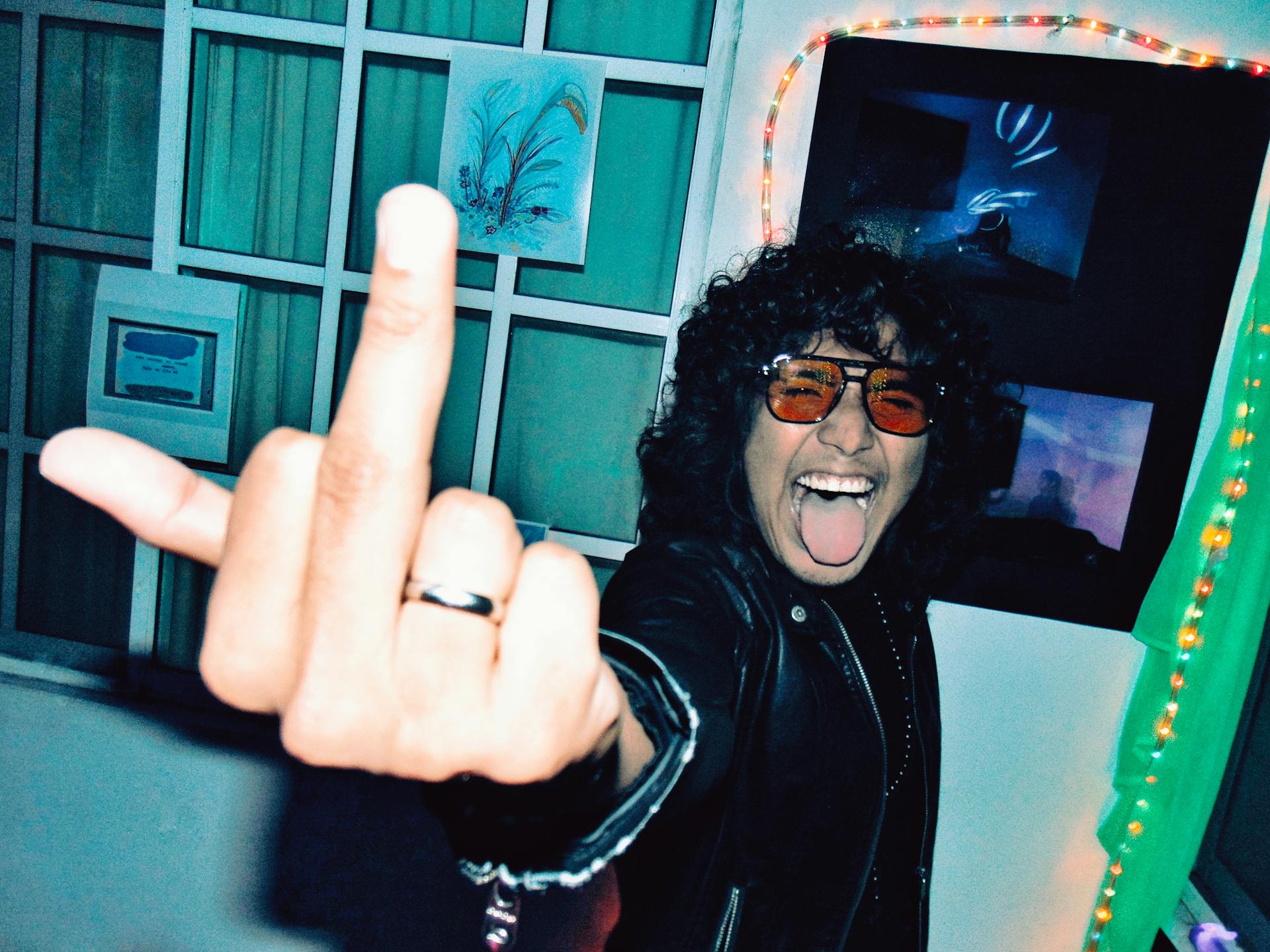 A person with curly hair and sunglasses expressing rebellion indoors with vibrant lighting.