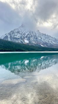 Serene lake reflecting a snowcapped mountain under cloudy skies, capturing natural tranquility.