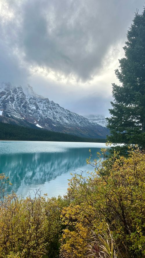 Free A serene mountain lake with snowy peaks and vibrant foliage, reflecting tranquil beauty. Stock Photo