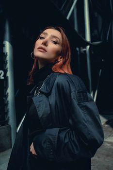 A fashionable woman in a dark jacket poses confidently in a moody urban background.