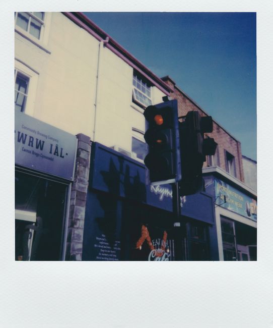 A vintage Polaroid of an urban traffic light with buildings in background, daytime.