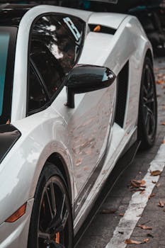 Close-up of a luxury white sports car parked on a city street with fallen leaves.