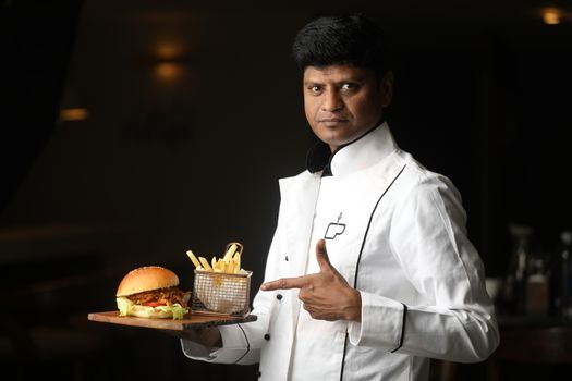 Chef showcasing a gourmet burger with fries in a stylish indoor setting.