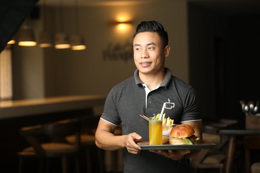 Male waiter presenting a burger and drink on a tray in an intimate Bengaluru restaurant setting.