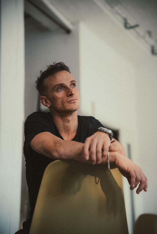 Free Man with thoughtful expression leaning on a chair indoors. Soft focus, moody lighting. Stock Photo