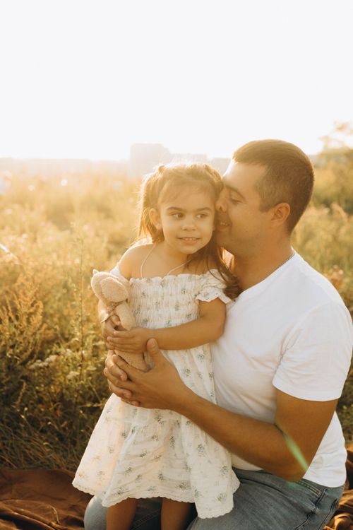 Free A father and daughter share a warm embrace in a sunlit field, capturing a tender moment. Stock Photo