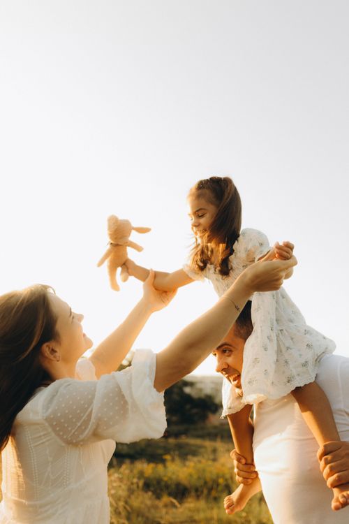 Free Joyful family bonding outdoors at sunset with parents lifting their daughter. Stock Photo