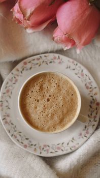 Top view of a frothy coffee cup with pink roses enhancing the elegant scene.
