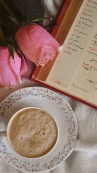 Pink roses, a cup of coffee, and an open book create a cozy morning vibe.