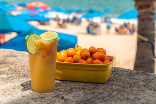 Tropical drink with lime and fresh fruits on a sunny beach, surrounded by umbrellas.