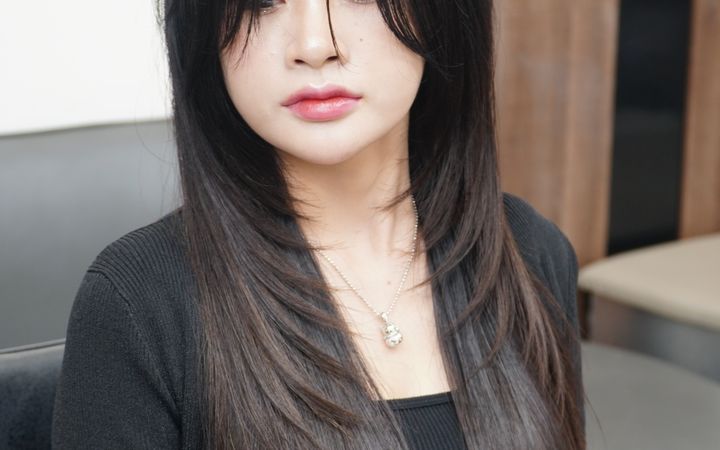 Portrait of a young woman with long straight hair sitting in a salon chair.