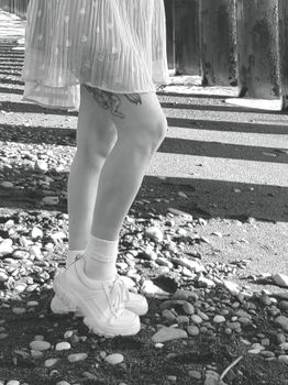 Close-up of legs in a skirt and sneakers on a pebble beach in black and white.