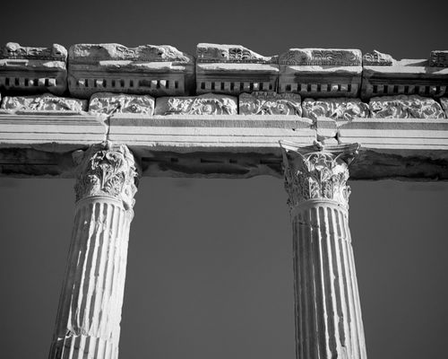 Free Monochrome photo of ancient Greek columns with detailed capitals against a clear sky. Stock Photo