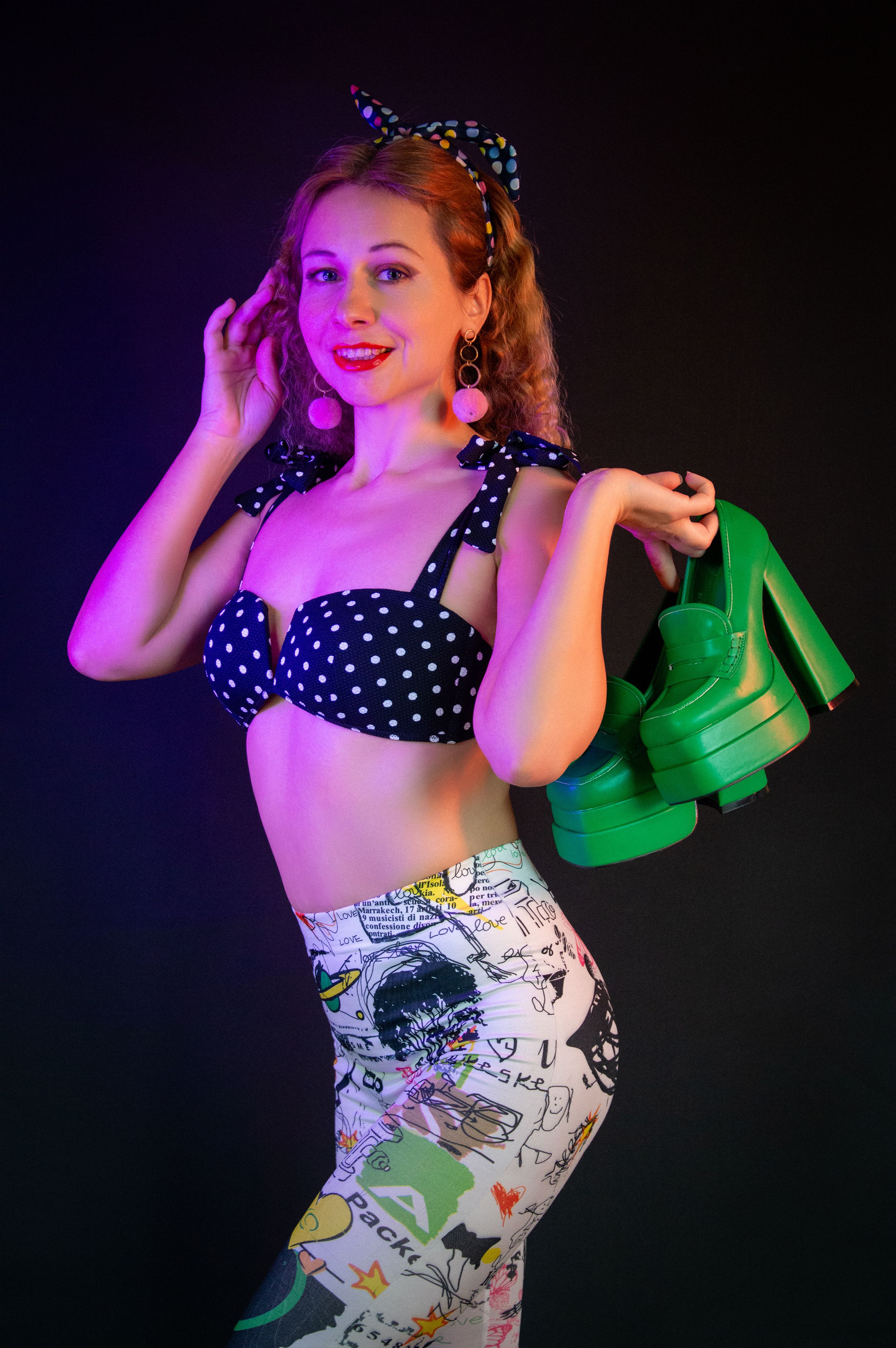 Fotomural Retrato vibrante de una mujer con moda retro sosteniendo zapatos verdes bajo una iluminación colorida.