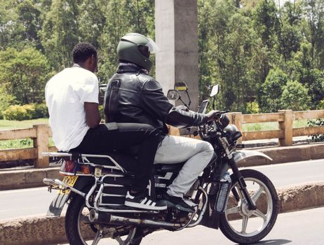 Two men on a motorcycle ride through Nairobi, showcasing urban transport and lifestyle.