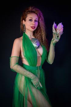 A woman in a green dress poses with a shell, showcasing elegance and style.