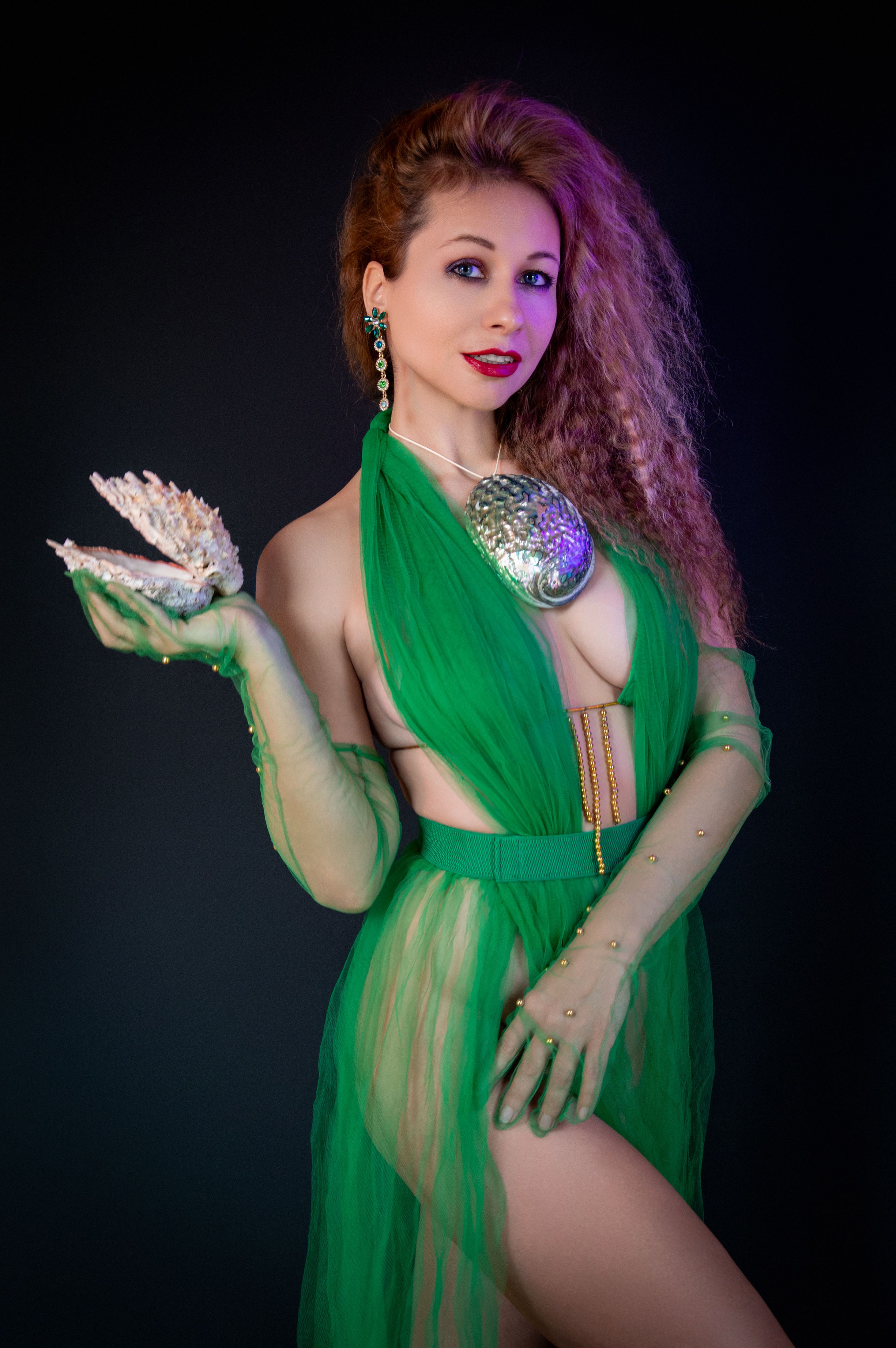 A stylish woman in a green dress holding a seashell, blending elegance with fantasy.