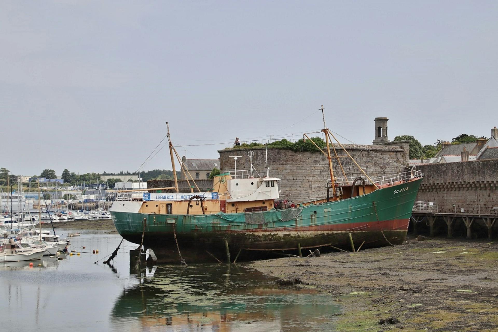 Rustic fishing boat docked at Concarneau harbor surrounded by old fort walls.