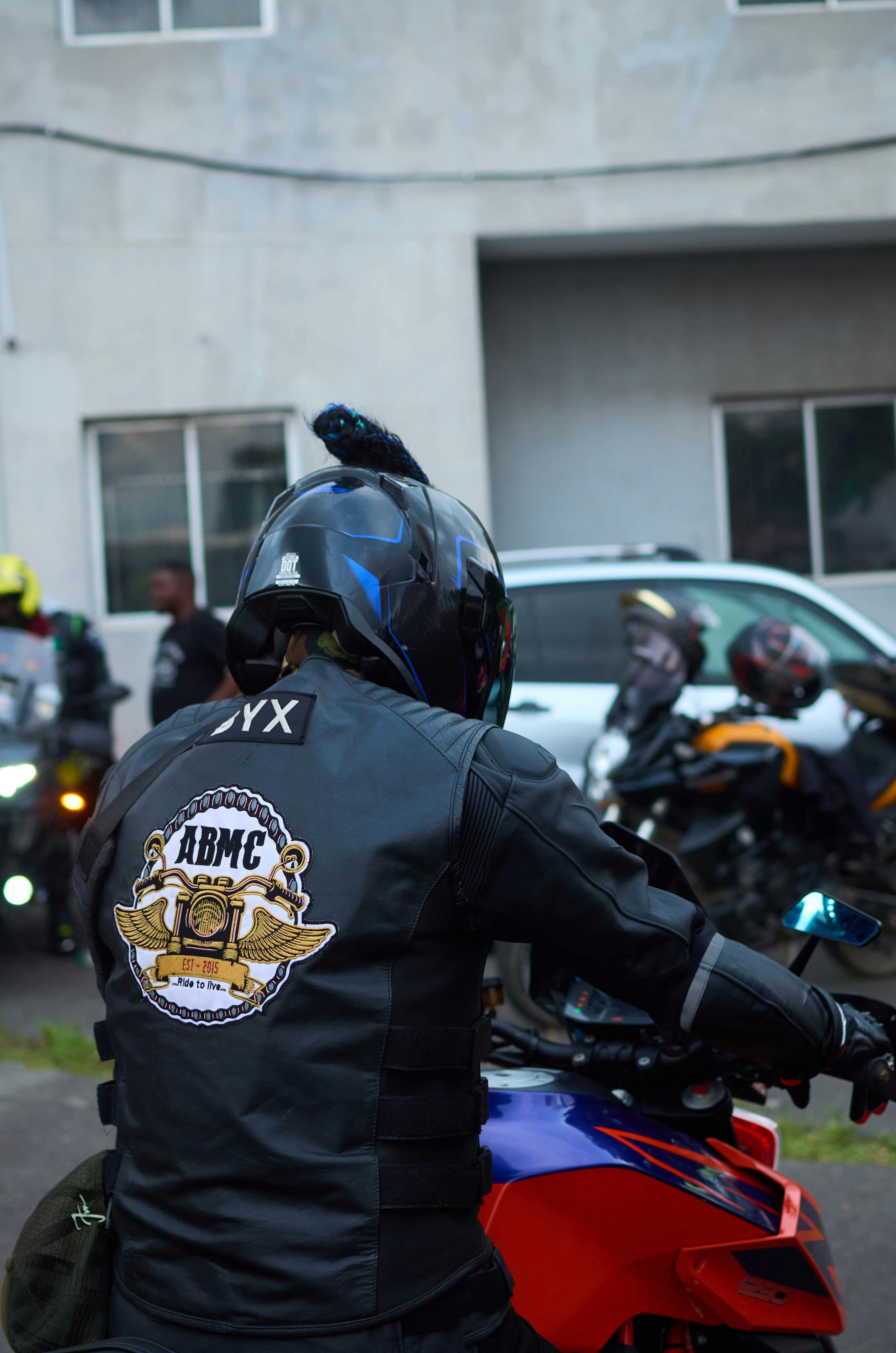 Rear view of motorcyclist wearing helmet, parked outside a building.