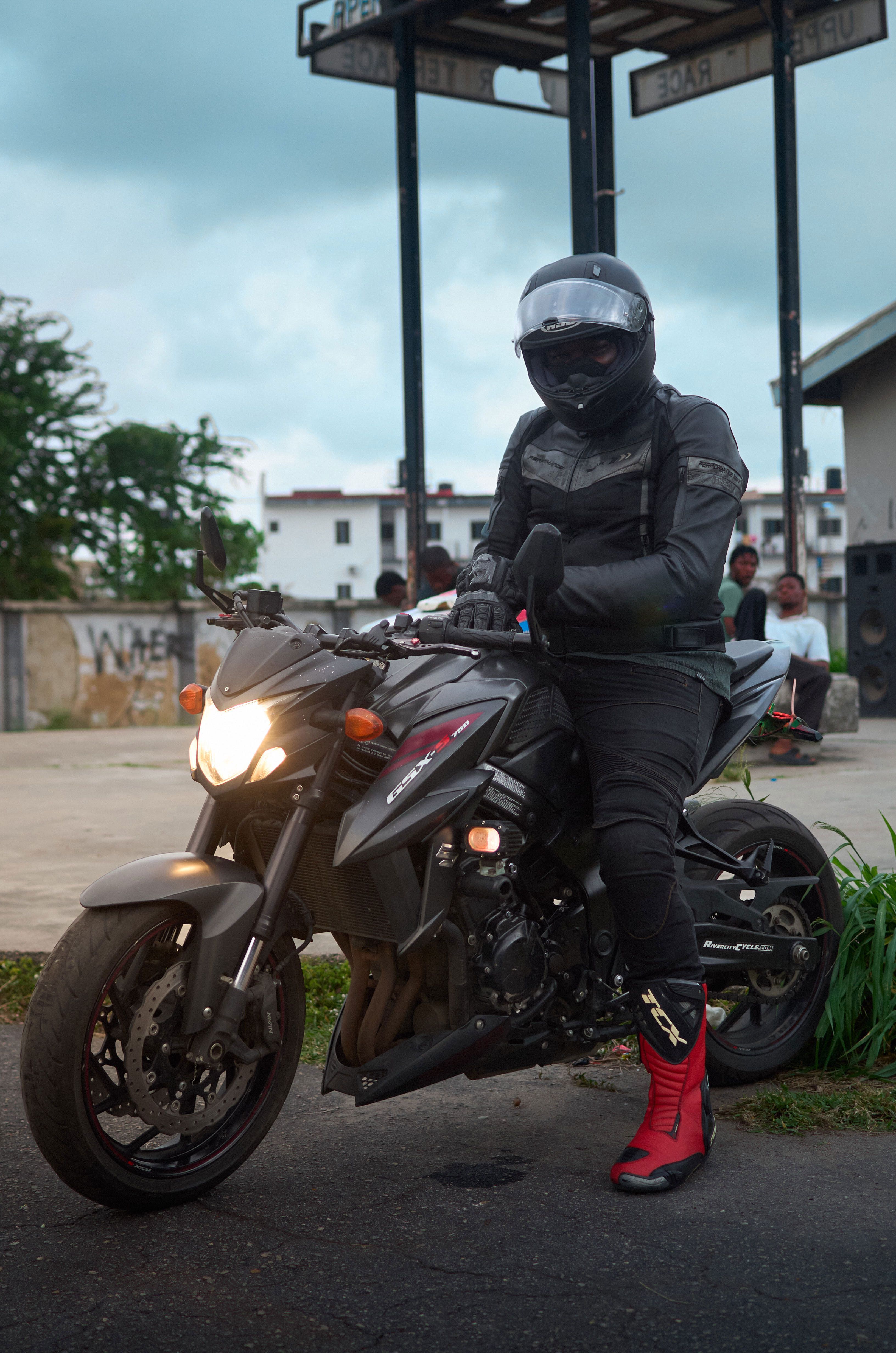 Motard en tenue complète noire, casque intégral, gants et bottes, assis sur sa moto