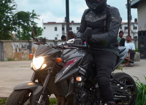 Motard en tenue complète noire, casque intégral, gants et bottes, assis sur sa moto