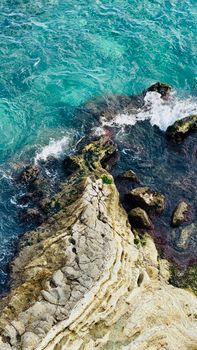 A stunning aerial capture of waves crashing onto a rocky shoreline with vibrant turquoise waters.