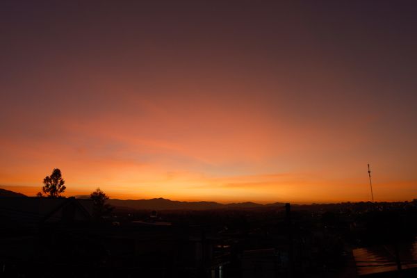 Um pôr do sol hipnotizante lançando tons coloridos sobre silhuetas urbanas e montanhas distantes.