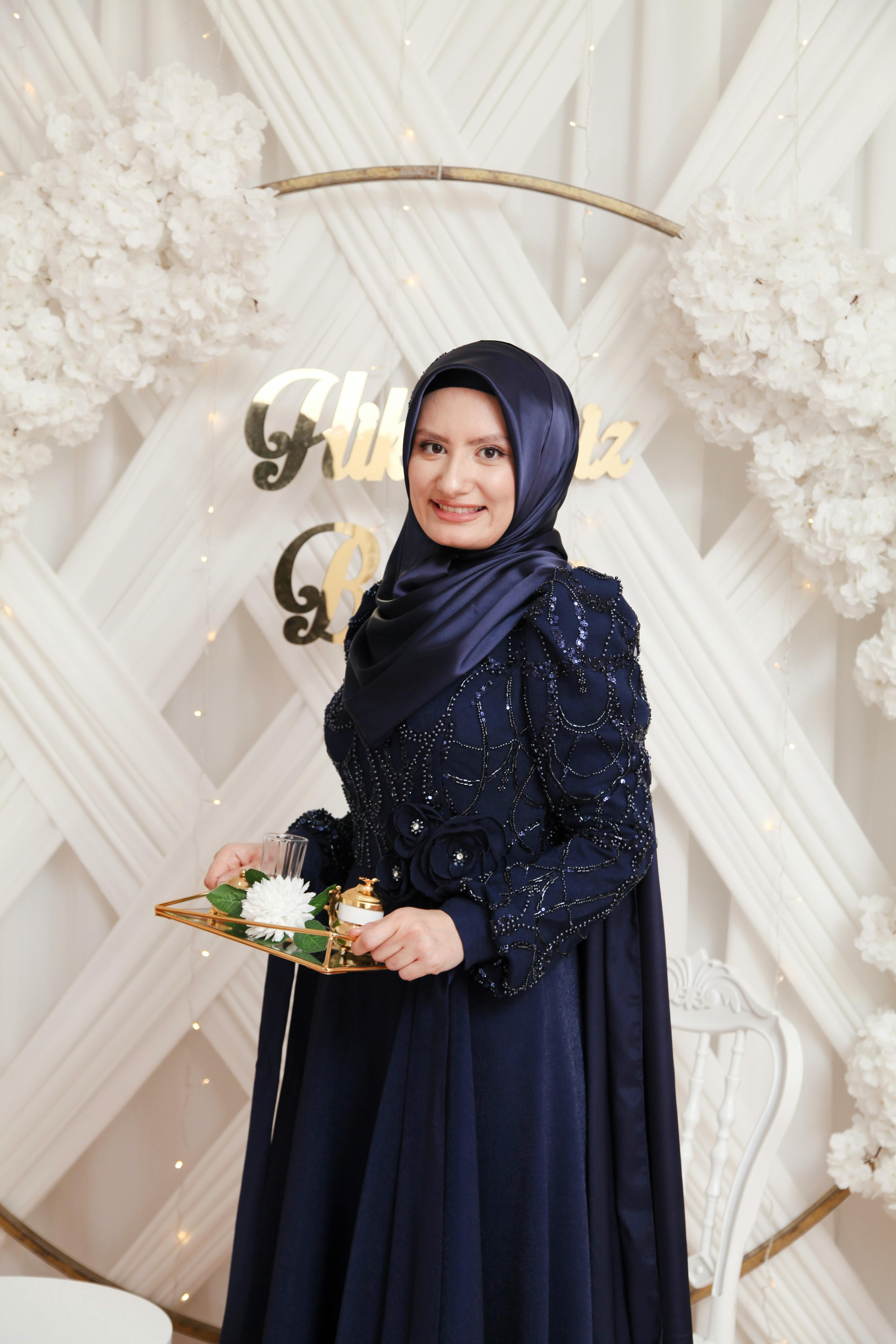 A woman in a stylish hijab holding a tray at a decorative ceremony