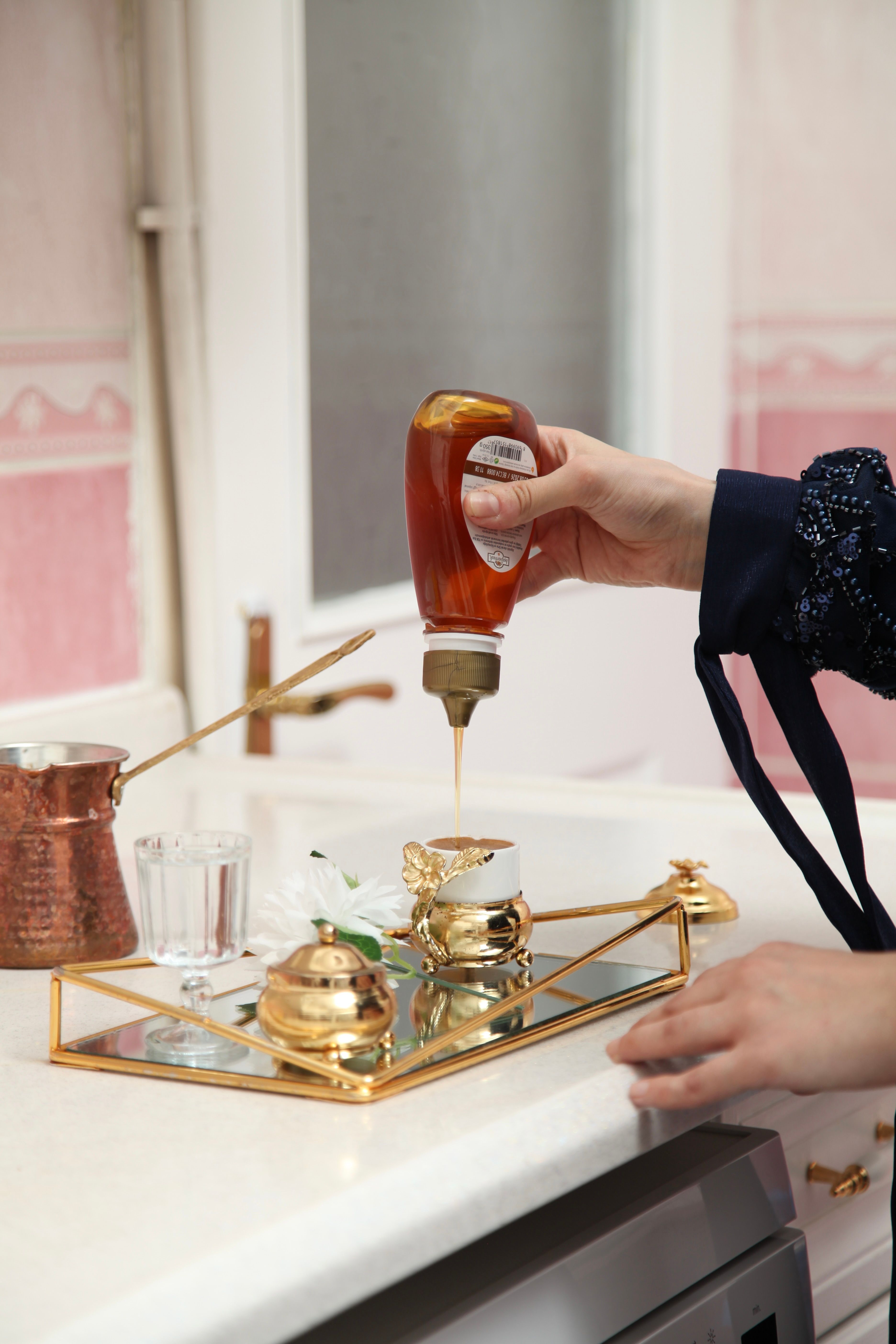 Woman pouring honey into a tea cup on an elegant tray with gold accents indoors.