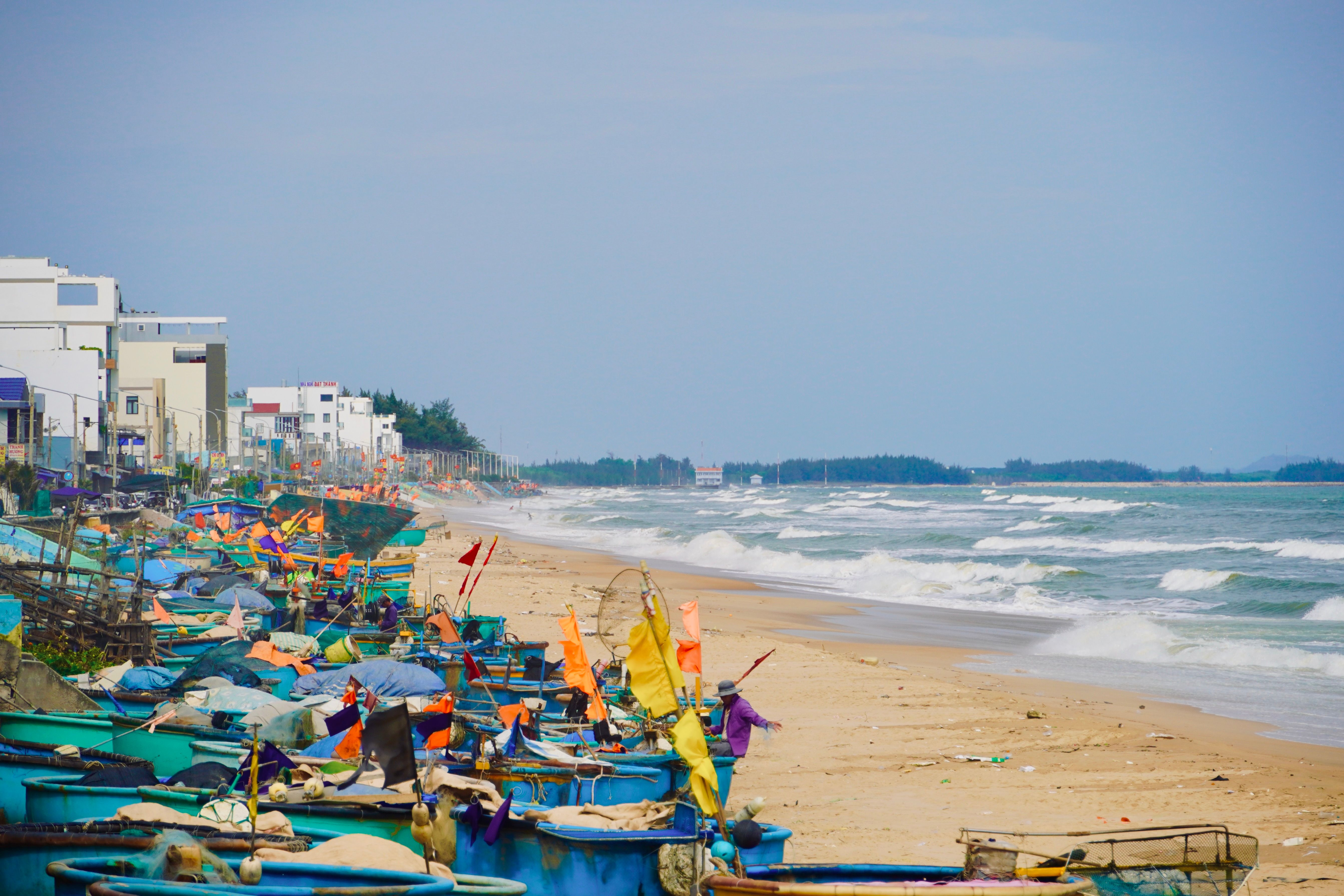 Vibrant fishing boats lined up on a sandy beach beside gentle ocean waves.
