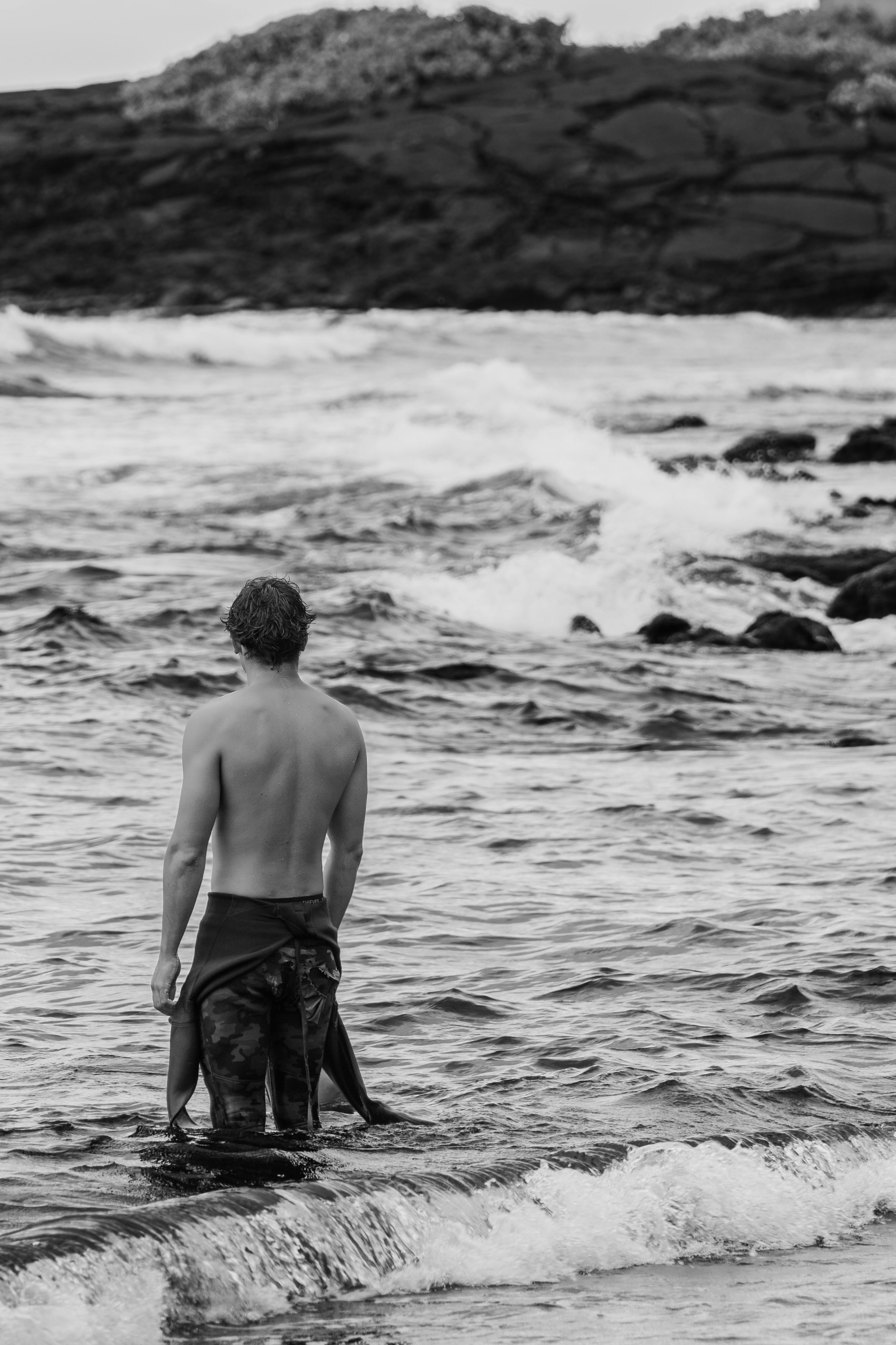 A lone surfer contemplates the surf on a Hawaiian beach, evoking solitude.