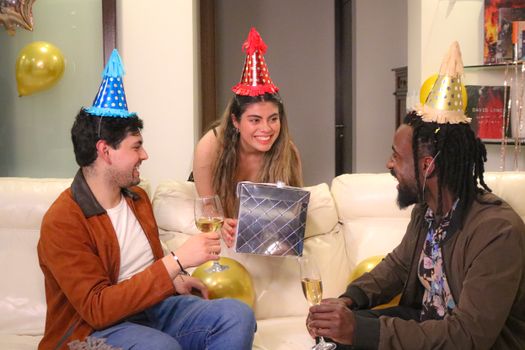 A cheerful group enjoying a birthday party with gifts and wine indoors.