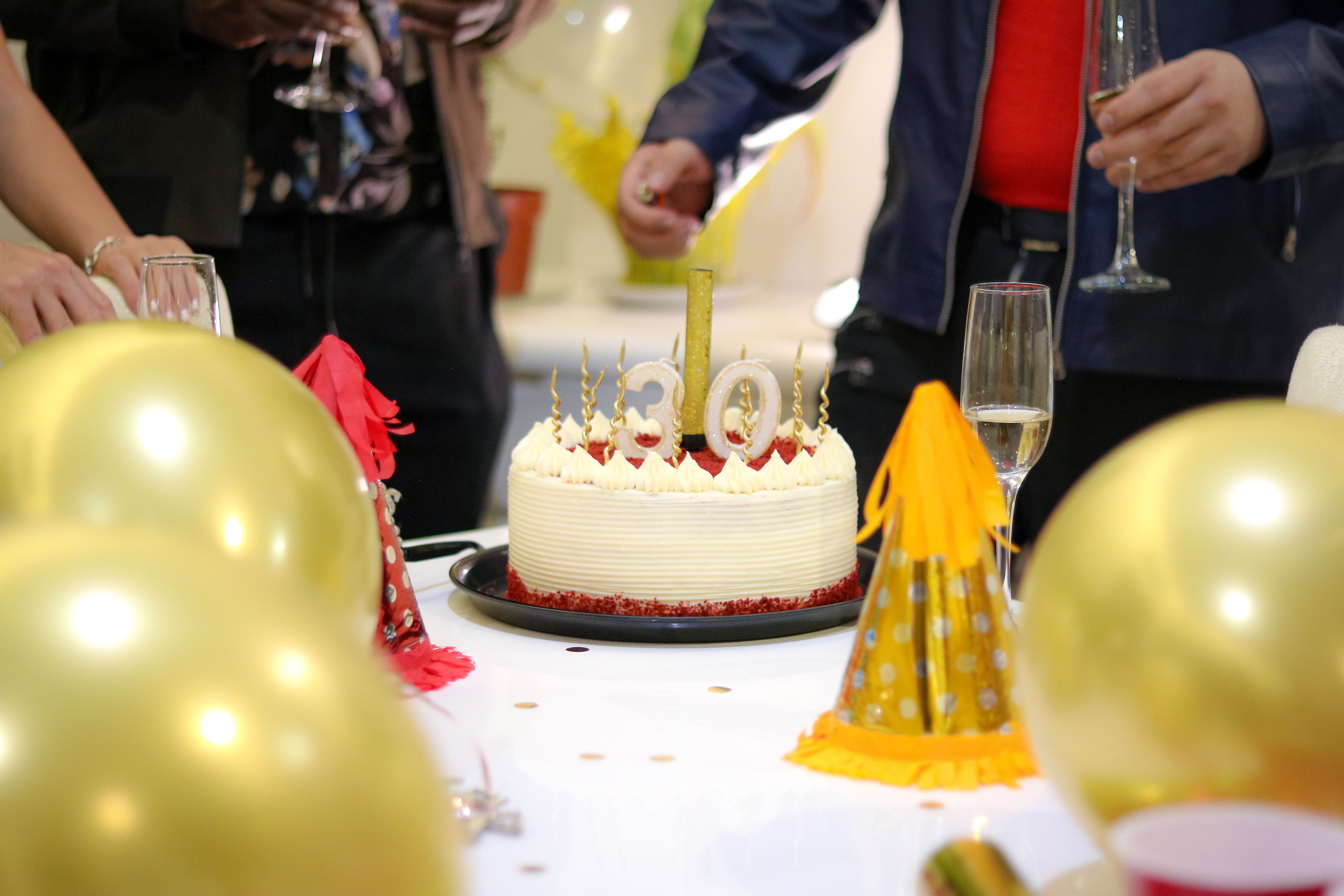 Elegant birthday party scene with a red velvet cake, golden balloons, and party hats.