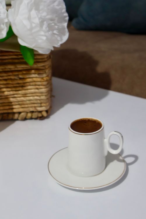 Free A minimalist ceramic coffee cup on a stylish white table with a decorative flower nearby. Stock Photo