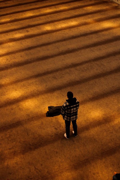 Free A lone man in a plaid jacket holding a coat standing on an illuminated patterned floor. Stock Photo
