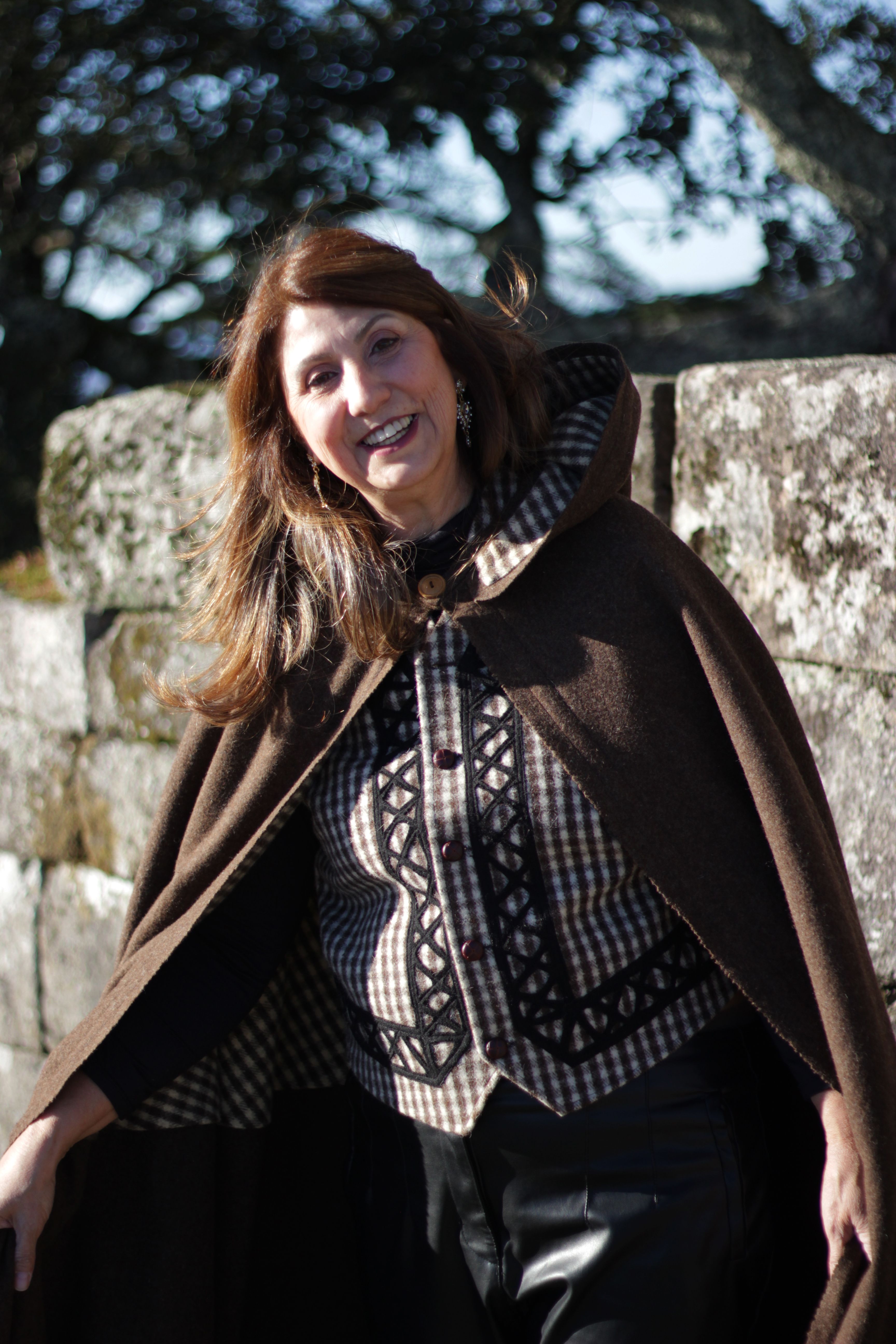 Smiling woman in traditional cloak outdoors by a stone wall in Portugal.