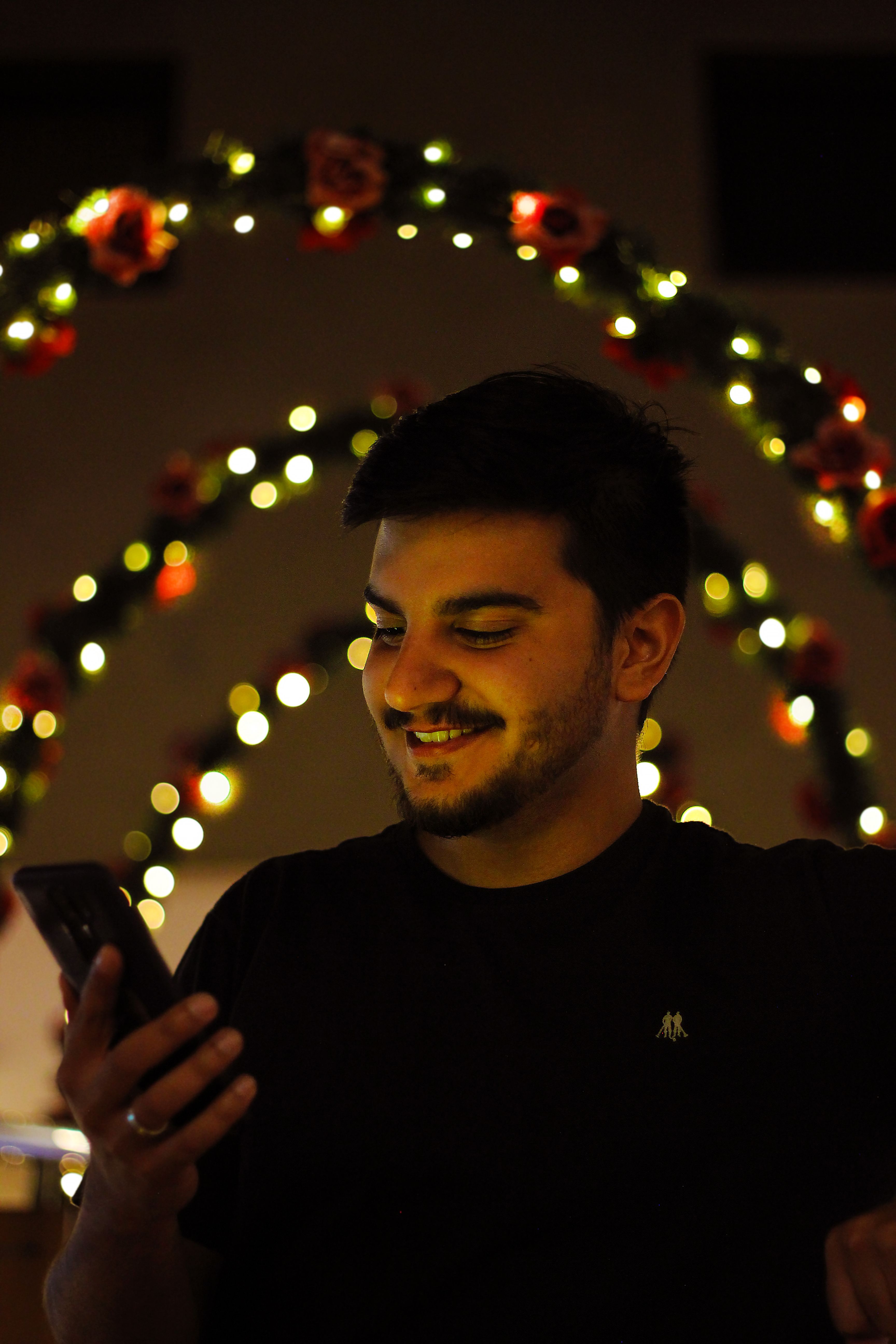Fotomural Joven sonriendo mientras usa su smartphone bajo luces festivas cálidas.