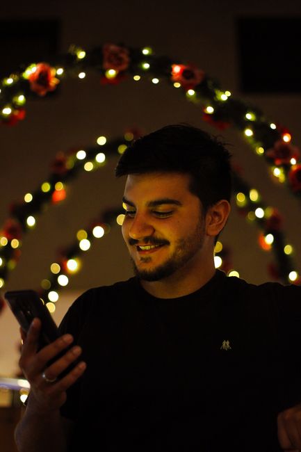 Fotomural Joven sonriendo mientras usa su smartphone bajo luces festivas cálidas.