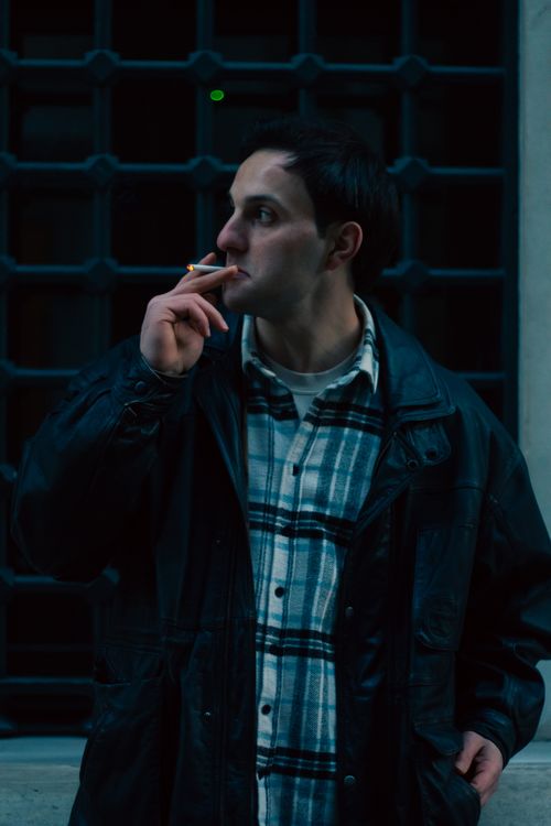 Free Portrait of a man smoking at night, wearing a leather jacket and plaid shirt in an urban setting. Stock Photo
