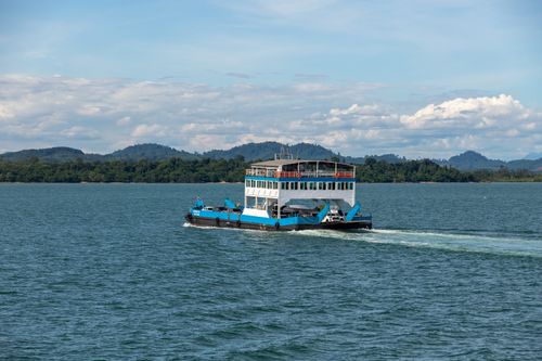 Free Passenger ferry traverses calm tropical waters with lush islands in the background under a clear blue sky. Stock Photo