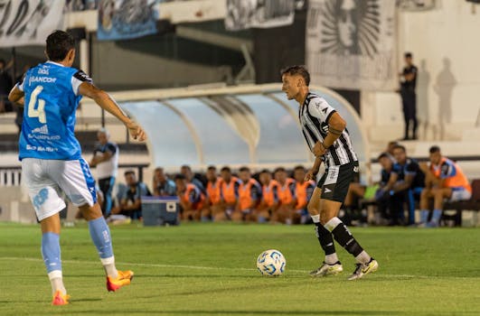 Players in blue and black uniforms compete in a lively soccer match on a green field.