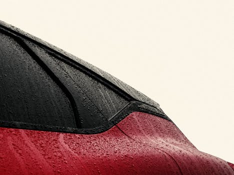 Close-up of a red car's window with rain droplets, showcasing a sleek design and reflective surface.