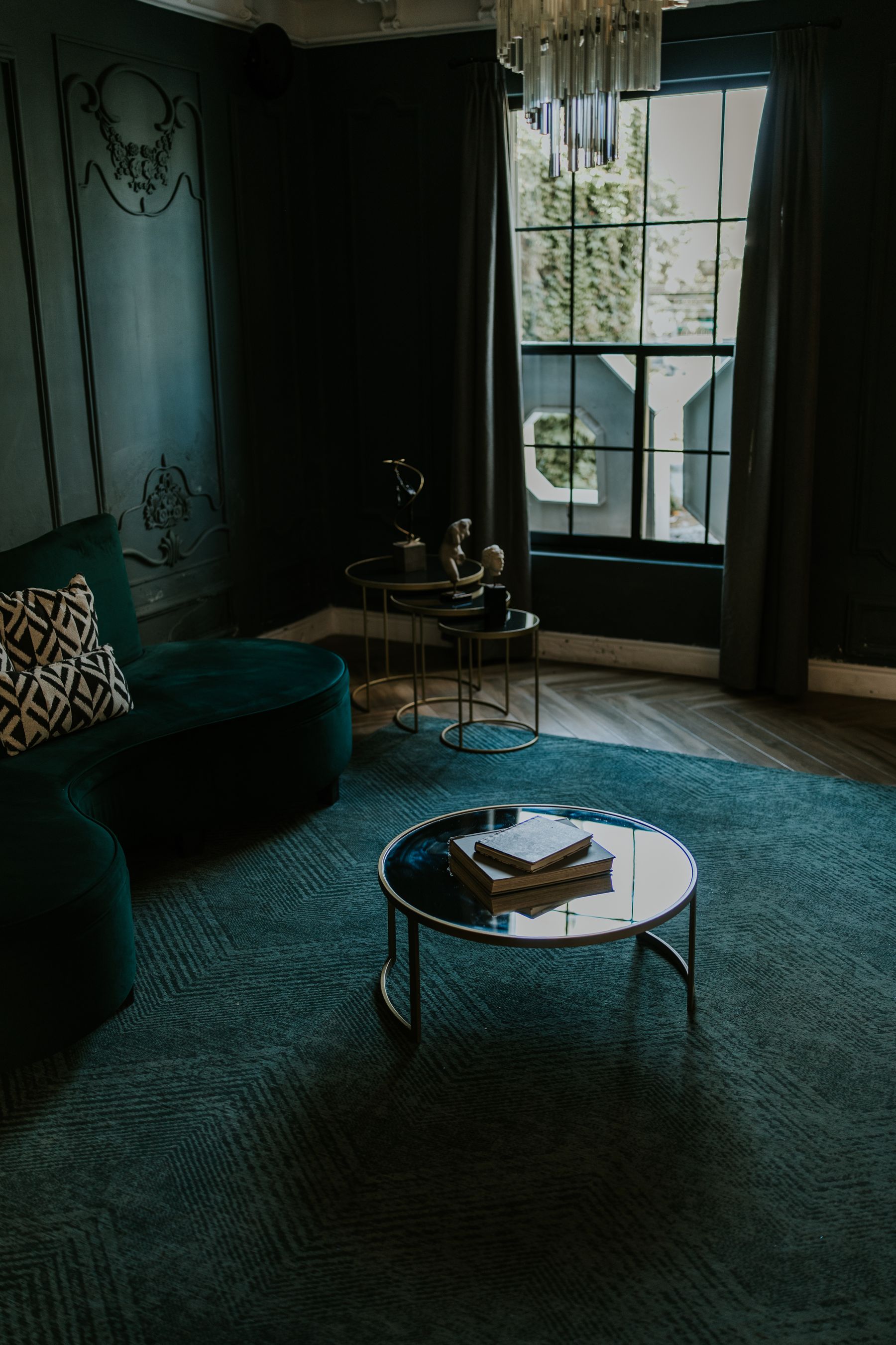 Dark green living room with paneled walls, velvet sofa, crystal chandelier and broad window