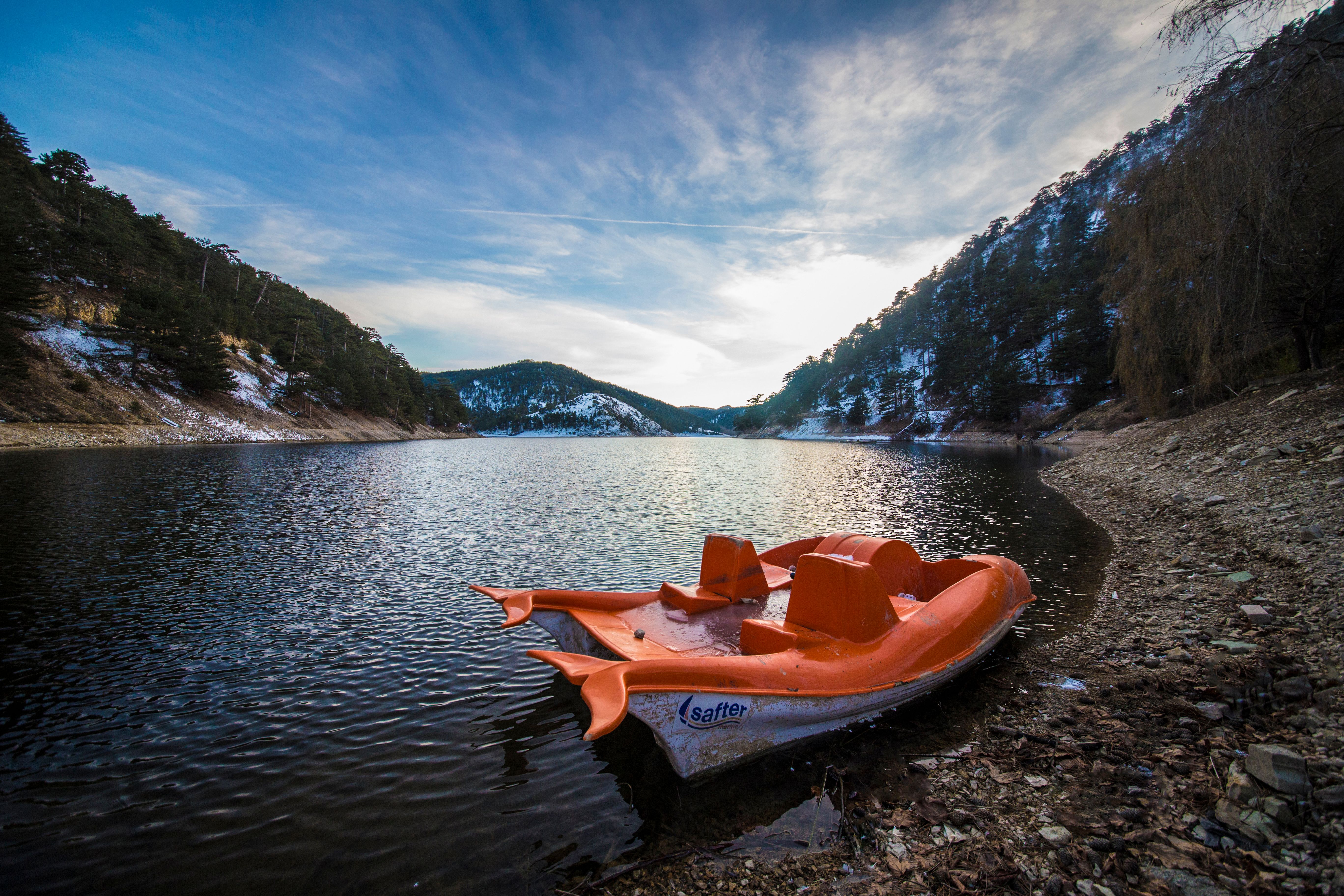An orange paddle boat rests on a calm lake surrounded by snow-covered hills in winter.