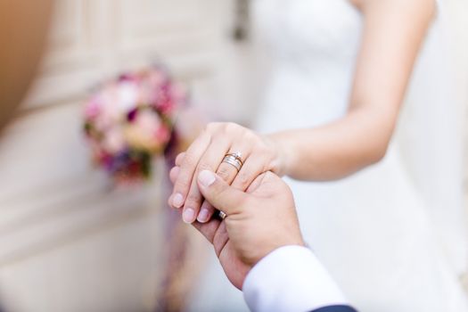 Bride and groom holding hands, focusing on wedding rings in a romantic moment.
