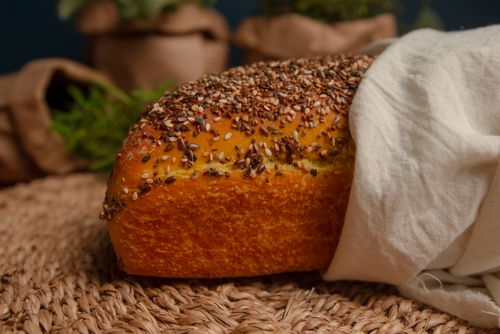 Free Close-up of a seeded bread loaf on a woven mat, partially covered by a cloth. Stock Photo